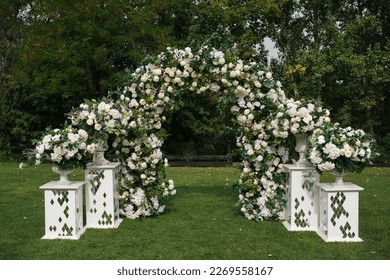 Wedding ceremony outdoor. A beautiful and stylish wedding arch, decorated by various fresh white flowers, standing in the garden. Celebration day.