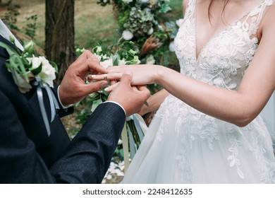 Wedding ceremony of putting on rings to the bride in a white dress and the groom with a boutonniere on a festive platform decorated with flowers in the afternoon close-up without faces