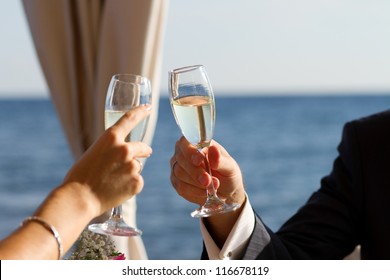 Wedding Champagne Toast.Bride & Groom Toasting With White Champagne Wine Glasses Outdoor On Wedding Day.Exotic Summer Resort Restaurant For Wedding Ceremony.Happy Newlyweds Hold Wedding Drinks Glasses