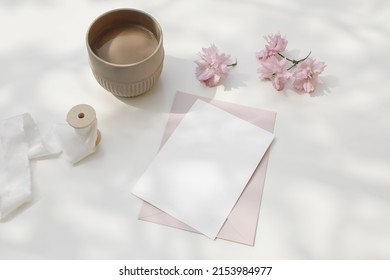 Wedding composition. Feminine spring breakfast still life. Pink Japanese cherry tree, sakura blossoms in sunlight. Blank greeting card, invitation. Cup of coffee. White dappled table background.