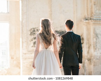 Wedding Couple Bride And Groom At Wedding Day Indoors At Old Church. Happy Marriage Couple Indoors, Soft Sunny Lights. Loving Man And Woman At Marriage Day. Back View