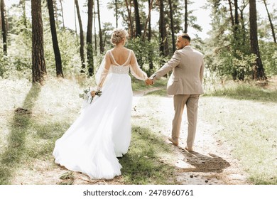 Wedding couple bride and groom walk hand in hand through a pine forest, sunlight filtering through the trees, highlighting their joyful expressions. - Powered by Shutterstock