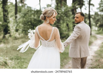 Wedding couple bride and groom walk hand in hand through a pine forest, sunlight filtering through the trees, highlighting their joyful expressions. - Powered by Shutterstock