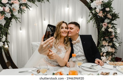 Wedding Couple Doing Silfi At The Wedding Table. Happy Lovers Are Photographed On The Phone During A Banquet. Wedding Feast. Holiday Food. Wedding Flowers And Decorations