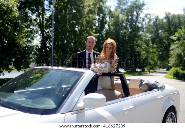 Wedding\
couple is hugging in a car. Beauty bride with groom. Beautiful\
model girl in white dress. Man in suit. Female and male portrait.\
Woman with lace veil. Cute lady and guy\
outdoors