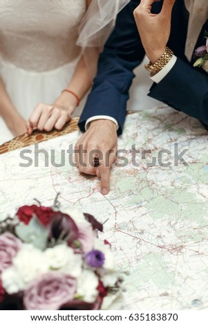 wedding couple planning honeymoon. stylish bride and groom looking at map, talking about summer travel vacation, sitting at wooden vintage table in cafe 