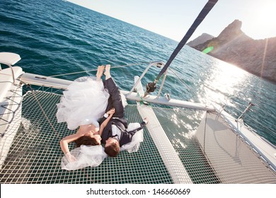 wedding couple relaxing on catamaran. Bride lying on a white wedding dress, groom in a dark suit