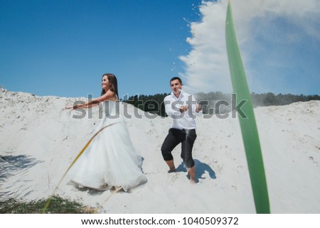 Wedding couple is running and jumping on the sandy lake beach. Funny laughing bride and groom in summer heat love story. Bride and groom are throwing sand. Travel lifestyle crazy emotional photo.