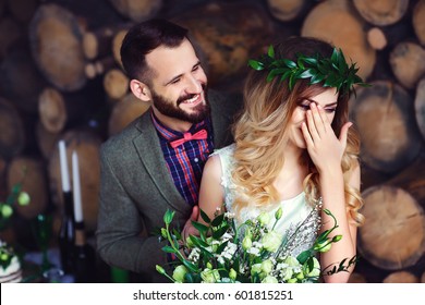 Wedding Couple Standing Near Wooden Logs. Groom Smiling, Bride Hiding Her Face And Laughing