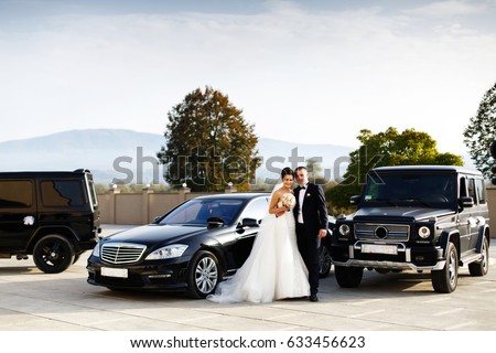 Wedding couple stands between E-clas and G-class Mercedes cars