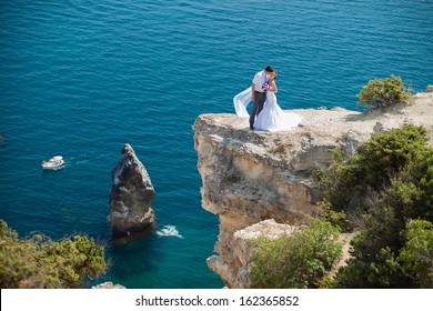 Wedding Couple Stands On A Cliff Above Blue Sea