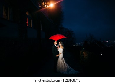 Wedding couple walk with red umbrella at night  - Shutterstock ID 1128108743