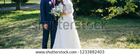 Wedding couple walking in the green park. Curvy bride in white lace dress and groom are holding hands. Overweight happy people. Love story outdoors. Beautiful bouquet.