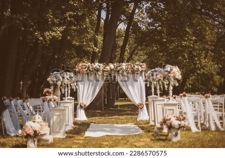 Wedding decor outside with flowers. Wedding ceremony. Arch, decorated with pink and white flowers standing in the woods, in the wedding ceremony area. Seats for guests at a beautiful wedding.