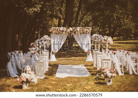 Wedding decor outside with flowers. Wedding ceremony. Arch, decorated with pink and white flowers standing in the woods, in the wedding ceremony area. Seats for guests at a beautiful wedding.