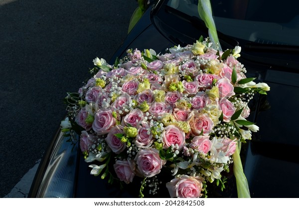 wedding decoration of a black\
sports limousine where the flower is attached with a suction cup to\
the hood. pink roses dominate the flat round bouquet. green\
ribbon