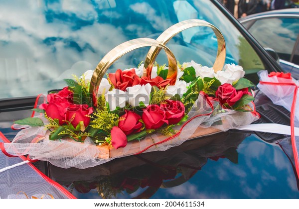 Wedding\
decoration of the car in the form of rings, artificial colors of\
red and white roses on the hood of the\
car.