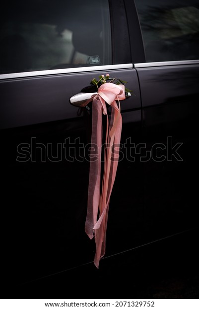 Wedding decorations on the doors of the wedding\
car. Flowers and pink\
ribbon.