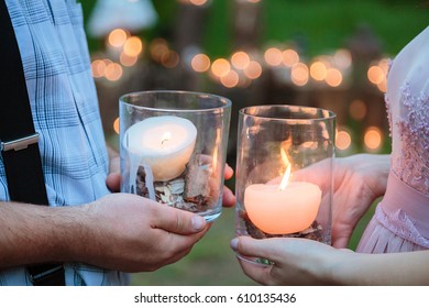 Wedding decorations in rustic style. Outing ceremony. Wedding in nature. Candles in decorated jars. Man and woman holding vases with burning candles