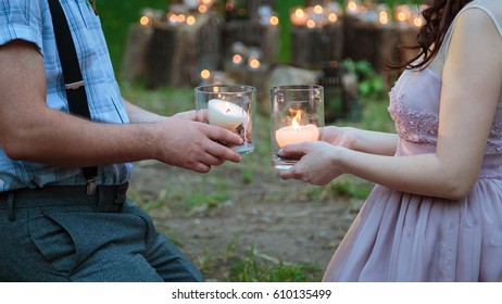 Wedding decorations in rustic style. Outing ceremony. Wedding in nature. Candles in decorated jars. Man and woman holding vases with burning candles