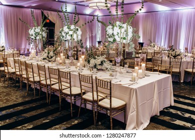 Wedding dinner table decor. Indian reception or banquet. Pastel and white colors. Long tables decorated with white flowers and golden cutlery.