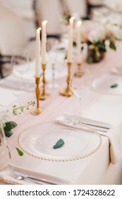 Wedding dinner table reception. Close-up of wildcard with gold beads, transparent glass. Runner of pink silk. Candles in golden candlesticks and flowers in the center of the table. 