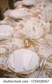Wedding dinner table reception. Delicate creamy pastel tones of tablecloths and plates on table, three forks left and two knives on right, glasses and candles in candlesticks