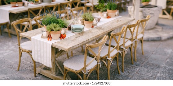 Wedding dinner table reception at sunset outside. Ancient rectangular wooden tables with rag runner, wooden vintage chairs, lavender pots, cherry tomatoes and clay pots with lemons on tables