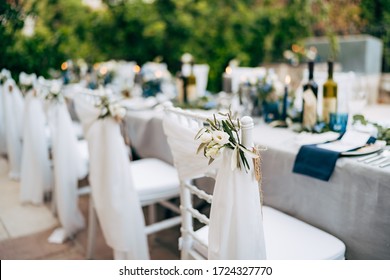 Wedding dinner table reception. White chair Chiavari Tiffany decorated with white delicate fabric and floral composition of white flowers, against the backdrop of the banquet table at the wedding