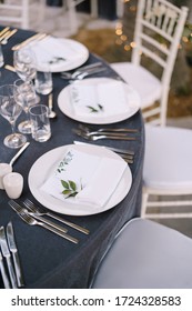 Wedding dinner table reception. White round plates on a round table with gray tablecloth, white Chiavari chairs with white pillows. A floral arrangement in the center of the table.