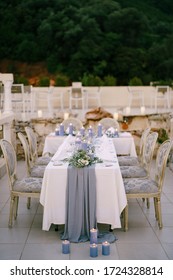 Wedding Dinner Table Reception. A White T-shaped Table With A Grey Tablecloth And Lots Of Blue Candles And Vintage Vintage Grey-gold Chairs Outside, On The Restaurants Summer Terrace.