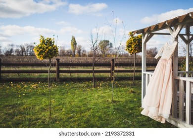 Wedding Dress Hanging On A Wooden Arbor.