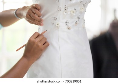 Wedding dressmaker designer working with mannequin in wedding dress with equipment.
