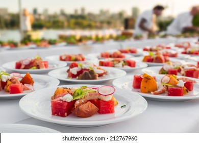 Wedding and event food preparation. Elegantly decorated by chef a salad with shrimp, water melon, reddish and fruits on the picnic table outdoors with an ocean view and city as a background 