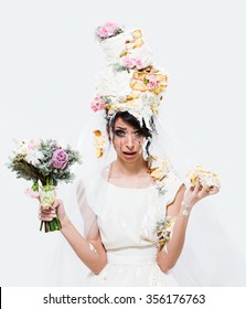 Wedding fail. Beautiful unhappy crying brunette bride with cake on her head on white background. Front view.