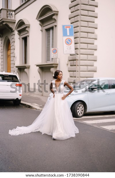 Wedding\
in Florence, Italy. African-American bride in a white dress, with a\
long veil, walks along the road on a city\
street.