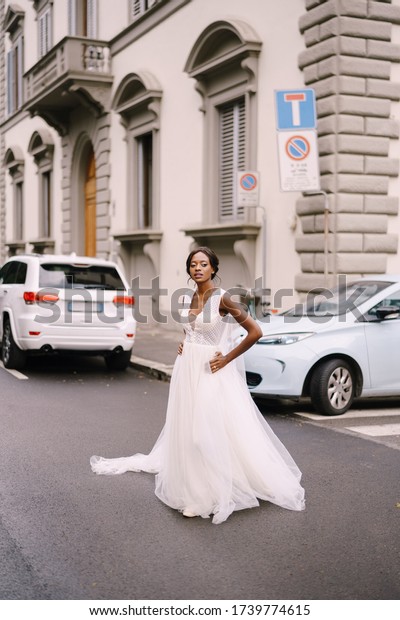 Wedding\
in Florence, Italy. African-American bride in a white dress, with a\
long veil, walks along the road on a city\
street.