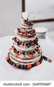 Wedding four-storey cake decorated with strawberries and forest fruits,completed with mint leaves and symbolic decorative hearts on top floor. The cake is on a silver tray and white fluffy tablecloth.