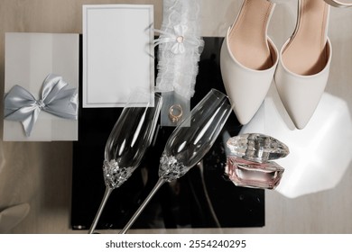 A wedding gift set with a white box, a ring, and two champagne flutes. The champagne flutes are placed on a table next to a white dress shoe - Powered by Shutterstock