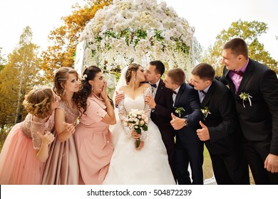 Wedding guests. Bride and groom kissing at wedding ceremony, bridesmaids and groomsmen looking at him, having fun and smiling