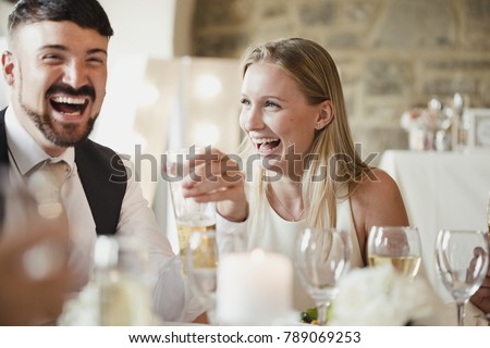 Wedding guests are enjoying themselves while sitting at the table for the meal. They are talking and laughing while drinking wine and lager.