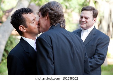 Wedding Of Handsome Gay Male Couple.  The Grooms Kiss As The Minister Looks On.