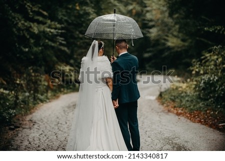 Wedding happy moments. A happy young couple, newlyweds walking the streets in rainy weather while carrying an umbrella. High-quality photo