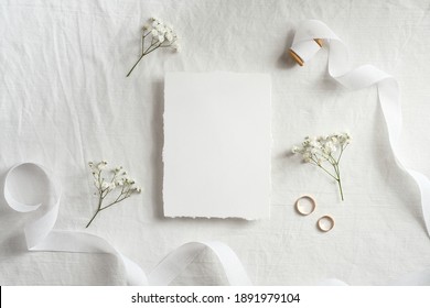 Wedding invitation card template. Top view blank paper card, ribbon, golden rings, flowers on white background. 