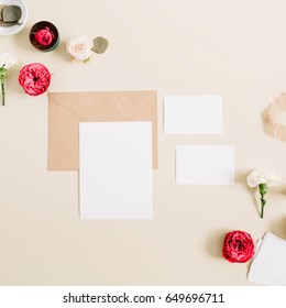 Wedding invitation cards, craft envelope, pink and red rose flower buds and white carnation on pale pastel beige background. Workspace with paper blank. Flat lay, top view - Shutterstock ID 649696711