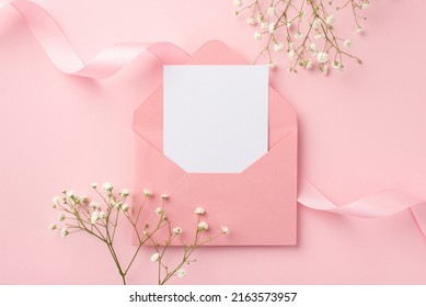 Wedding invitation concept. Top view photo of open pink envelope with paper card pink curly ribbon and white gypsophila flowers on isolated pastel pink background with empty space