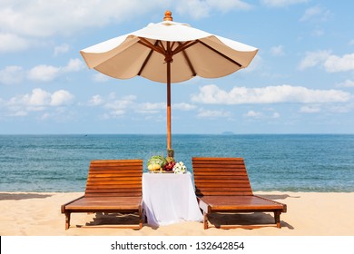 Wedding lunch on a sandy beach. Two loungers, parasol and a table with fruit.