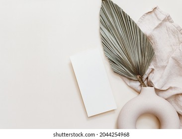 Hochzeitsmoor. Blank Grußkarte und grüne Palmenblätter. Keramikvase auf beigem, neutralem Hintergrund. Flachlage, Draufsicht. Mittelmeer, Sommerdesign.