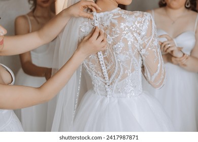 Wedding morning. Bridesmaids help put on the white wedding dress. A young woman is preparing to meet her groom and having fun with her friends