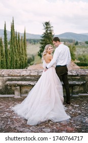 Wedding At An Old Winery Villa In Tuscany, Italy. A Wedding Couple Stands On The Roof Of An Old Winery, Cuddles, Stands With His Back To The Frame.